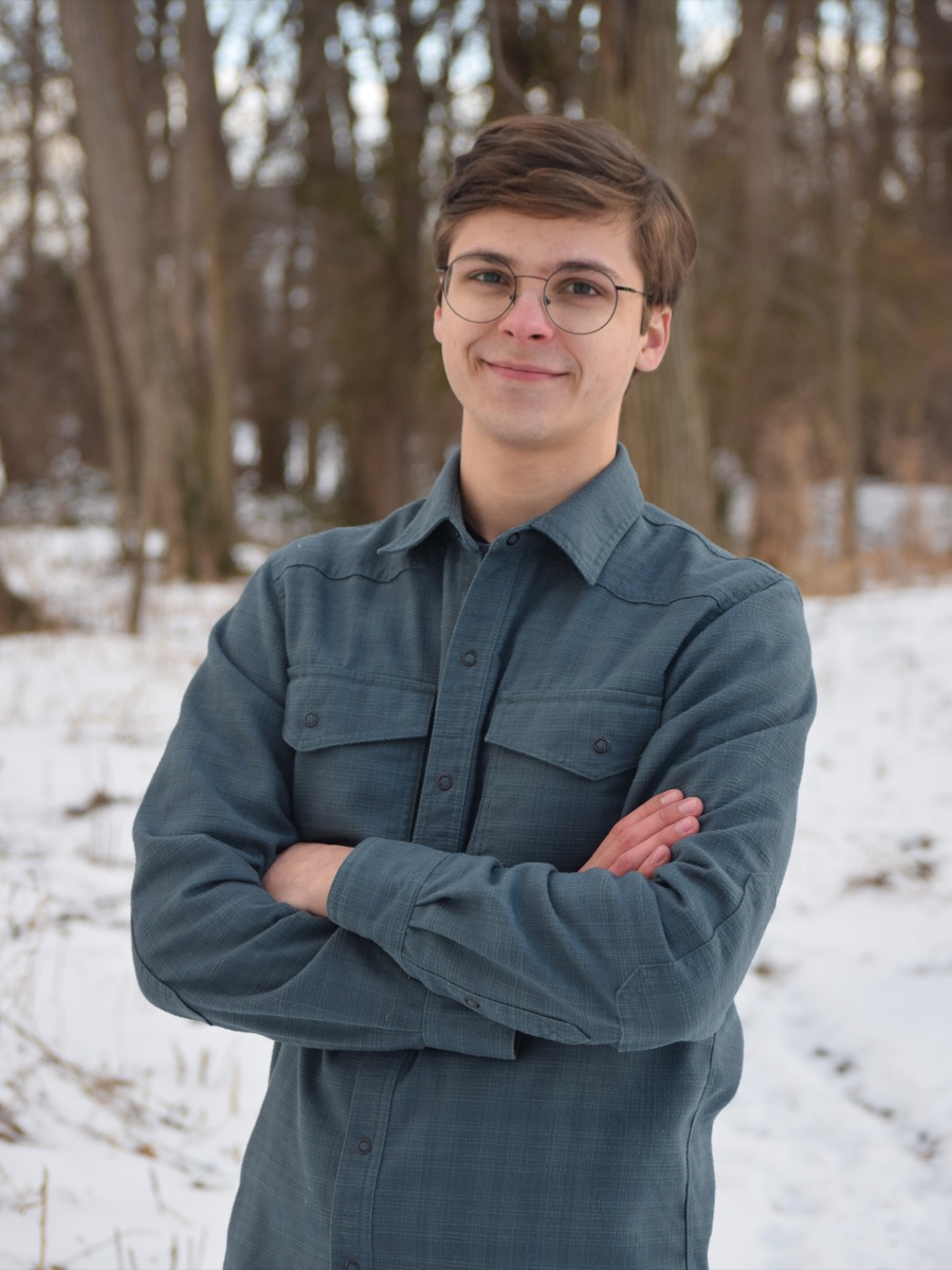 Samuel van Vuuren — in a snowy woodland, teal shirt, round glasses